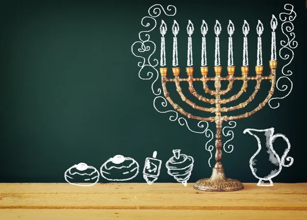 Image of jewish holiday Hanukkah with drawing menorah candles (traditional Candelabra), donuts and dreidels (spinning top) over chalkboard background.