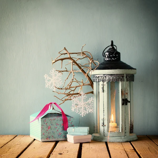 White wooden vintage lantern with burning candle christmas gifts and tree branches on wooden table. retro filtered.