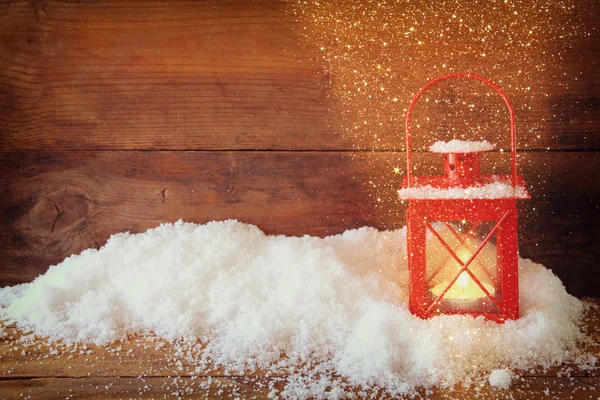Christmas background with red lantern ans snow over wooden background with glitter overlay.