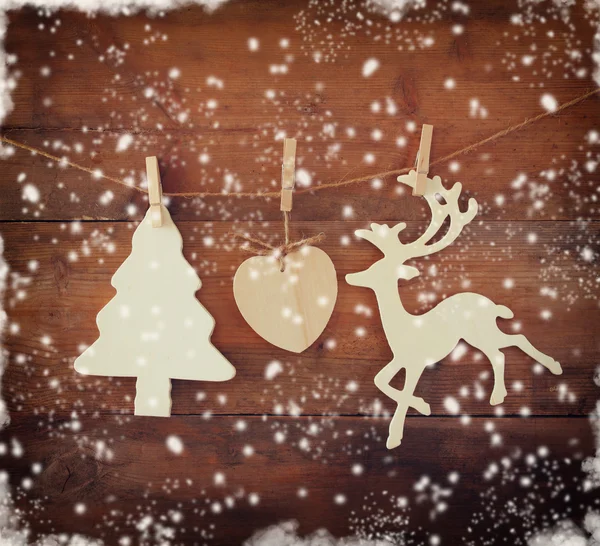 Image of wooden decorative christmas tree and reindeer hanging on a rope over wooden background with abstract snow overlay.