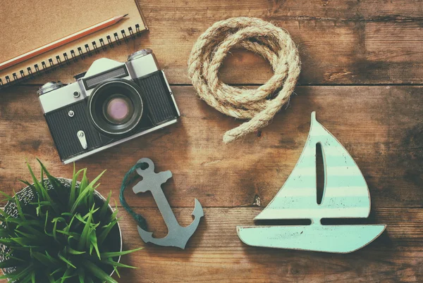 Retro filtered image of top view image of blank notebook, wooden sailboat, nautical rope and camera. travel and adventure concept