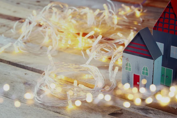 Decorative house next to gold garland lights on wooden background. copy space.