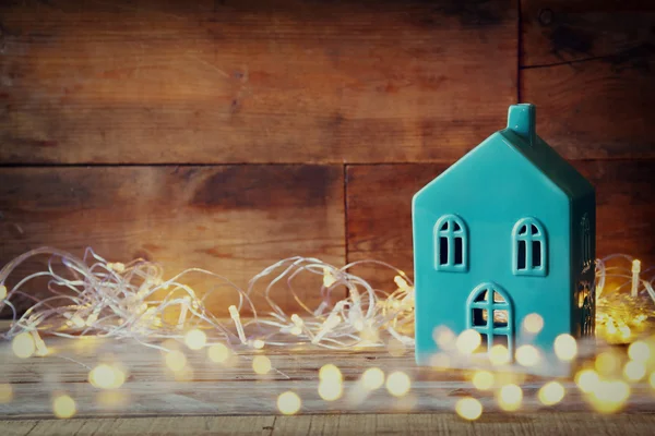 Photo of decorative house next to gold garland lights on wooden background. copy space. retro filtered.