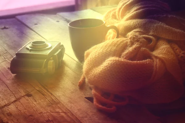 Selective focus photo of pink cozy knitted scarf with to cup of coffee next to old photo camera on a wooden table. photographed without editing software, using handmade filter.