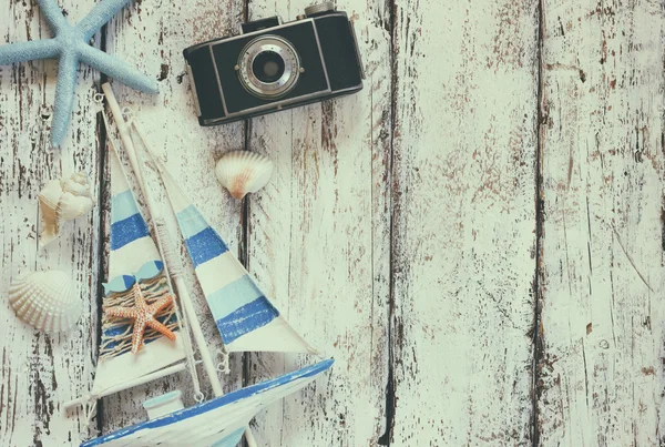 Top view image of photo camera, wood boat, sea shells and star fish over wooden table