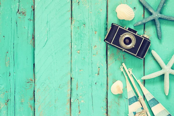 Top view image of photo camera, wood boat, sea shells and star fish over wooden table