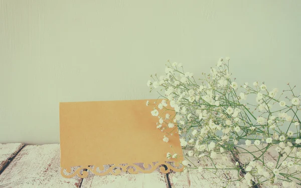 Fresh white flowers next to vintage empty card over wooden table. vintage filtered and toned image