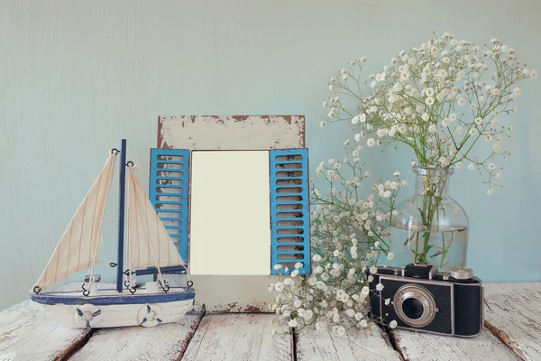 Old vintage wooden frame, white flowers, photo camera and sailing boat on wooden table. vintage filtered image. nautical lifestyle concept. template, ready to put photography
