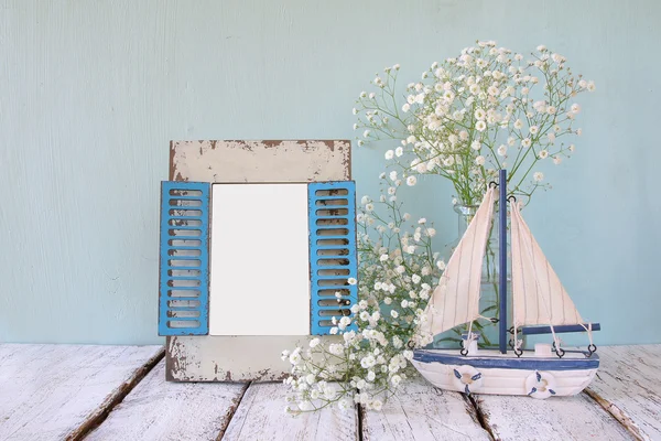 Old vintage wooden frame, white flowers and sailing boat on wooden table. vintage filtered image. nautical lifestyle concept. template, ready to put photography