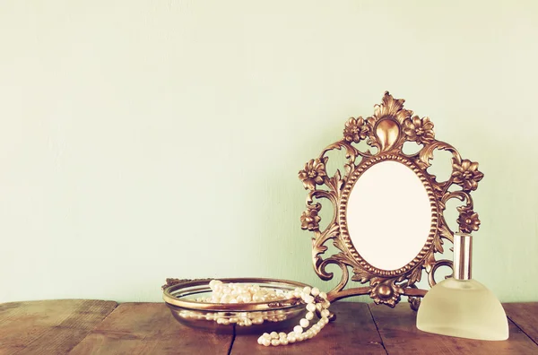 Antique blank victorian style frame, perfume bottle and white pearls on wooden table. retro filtered and toned. template, ready to put photography