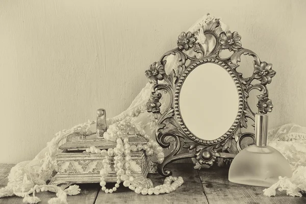 Antique blank victorian style frame, perfume bottle and white pearls on wooden table. black and white style photo. template, ready to put photography