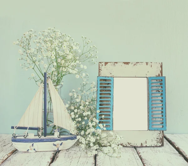 Old vintage wooden frame, white flowers and sailing boat on wooden table. vintage filtered and toned image. nautical lifestyle concept. template, ready to put photography