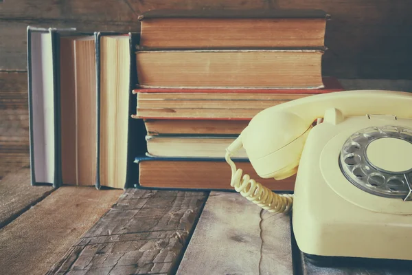 Vintage dial phone next to stack of old books over wooden table