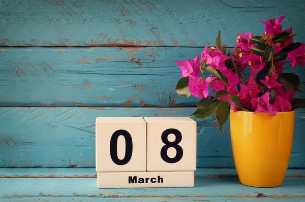 Wooden March 8 calendar, next to purple flowers on old blue rustic table. selective focus. vintage filtered