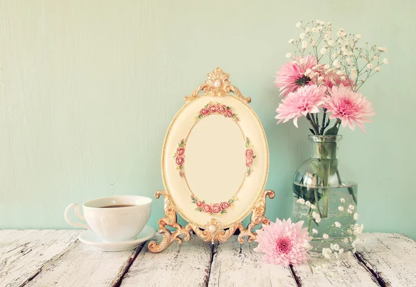 Vintage perfume bottle next to pink and white flowers and antique frame on wooden table. vintage filtered