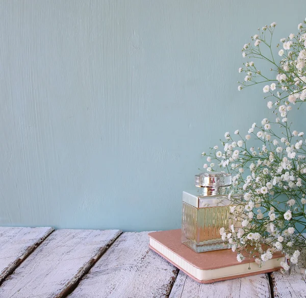 Vintage perfume bottle and notebook next to white flowers on wooden table