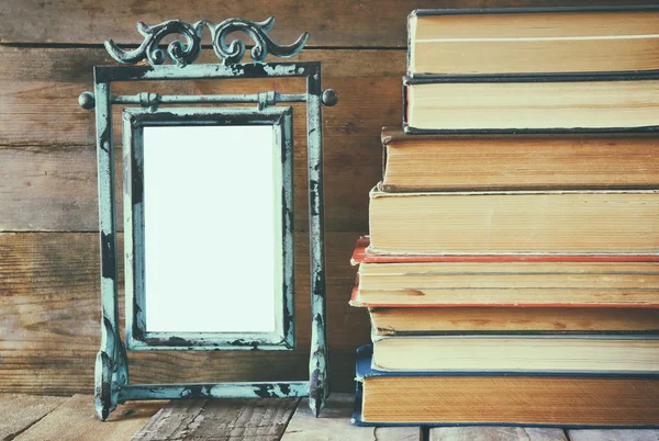 Stack of old books next to vintage blank frame wooden table. vintage filtered image