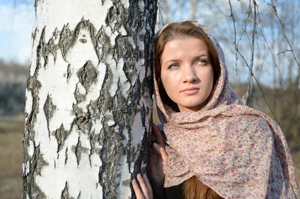Russian girl in a scarf in a birch forest close up