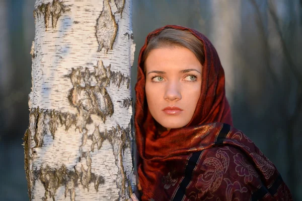 Russian girl in a scarf in a birch forest, close-up