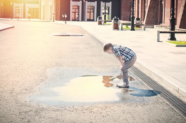 Little boy is looking at the puddle