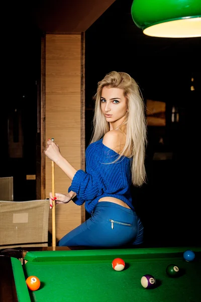 Hot young blonde woman posing on the pool table with the cue