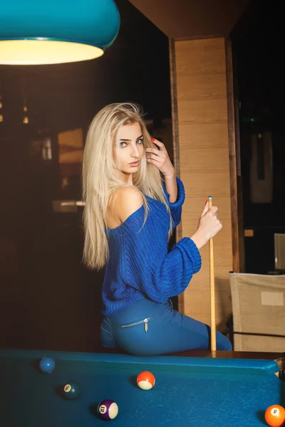 Sensual young blonde lady posing on pool table with the cue