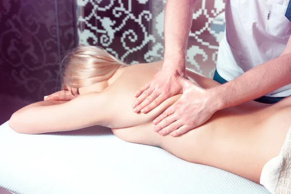 Man makes a back massage for a young blonde woman