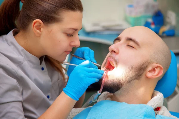 Dentist examining a patients teeth in the dentists chair under b