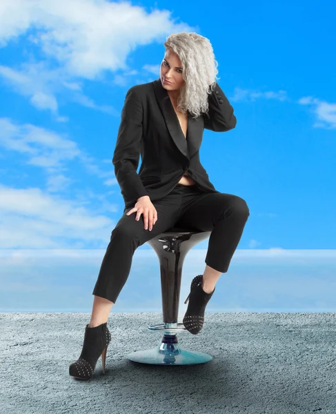 Woman with blue eyes sits on chair in black business suit