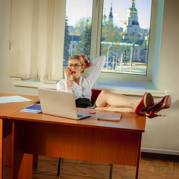 Beautiful secretary sitting at a desk and talking on a mobile