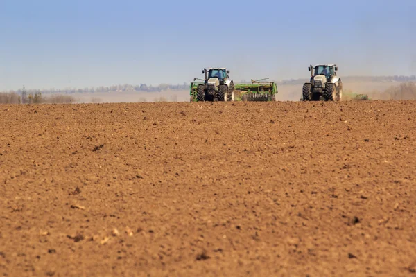 Two tractors sowing in field