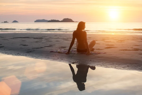 Woman sitting on the beach in the setting sun. Silhouette, the reflection in the water.