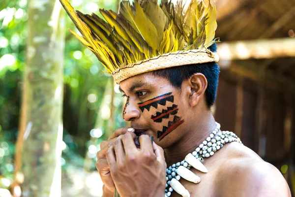 Native Brazilian guy playing wooden flute at an indigenous tribe in the Amazon