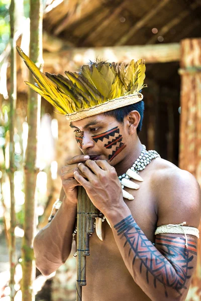 Native Brazilian guy playing wooden flute at an indigenous tribe in the Amazon