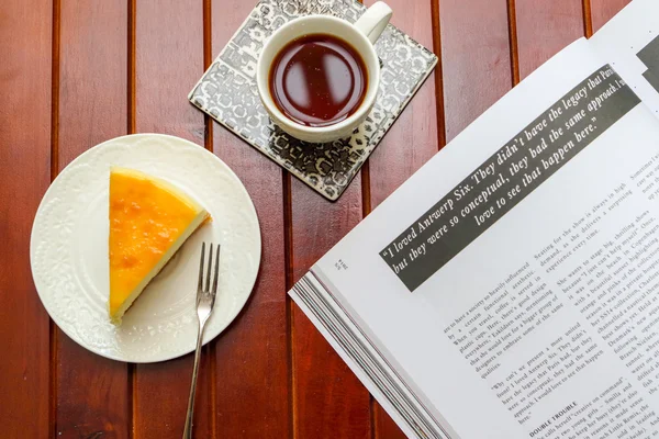 Opened Book on wooden table with cup of black coffee and sliced cheese cake
