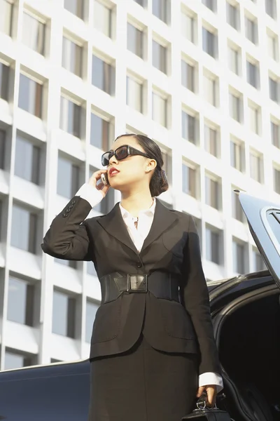 Asian businesswoman using cell phone next to car