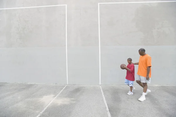 African man and son with basketball on outdoor court