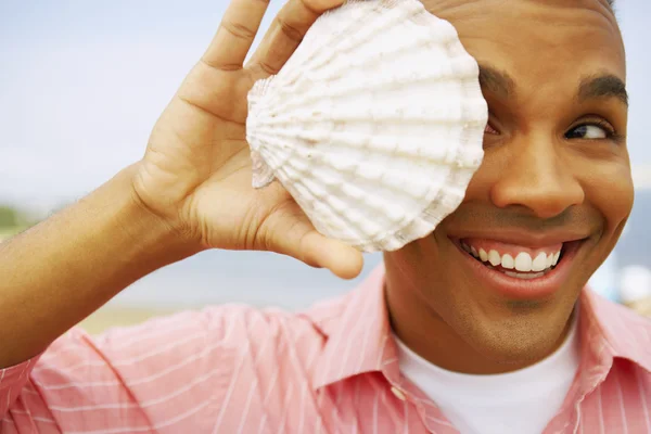 Hispanic man holding seashell over eye