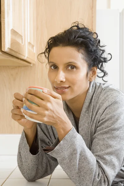 Indian woman drinking coffee in kitchen