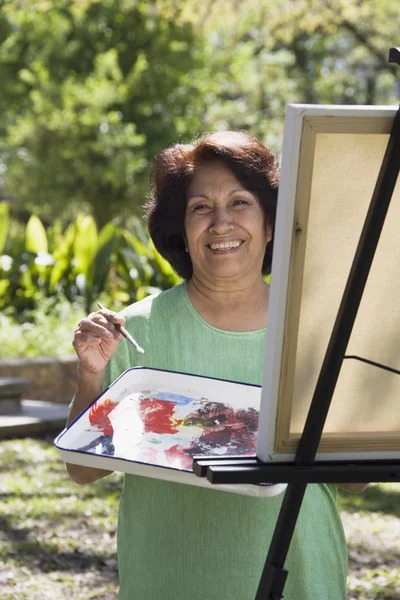 Senior Hispanic woman painting with easel outdoors