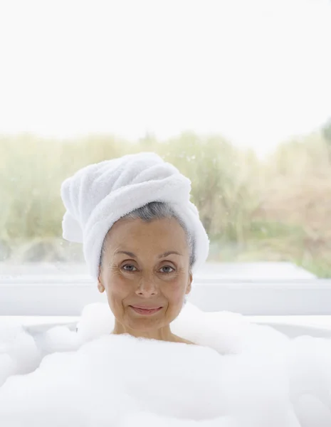 Elderly woman in bubble bath with towel wrapped around head