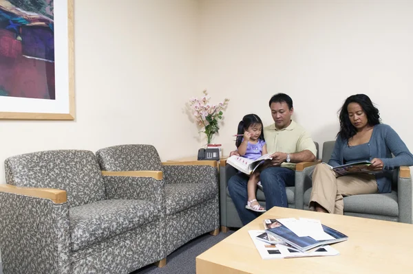 Family reading magazines in waiting room