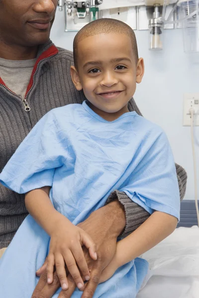 African boy in hospital gown sitting on father\'s lap