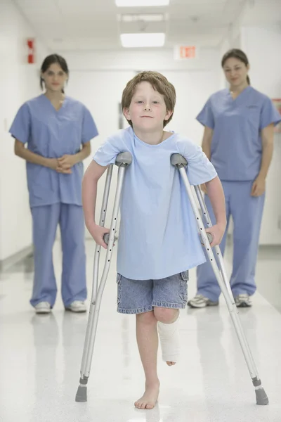 Nurses watching boy with broken leg walk with crutches