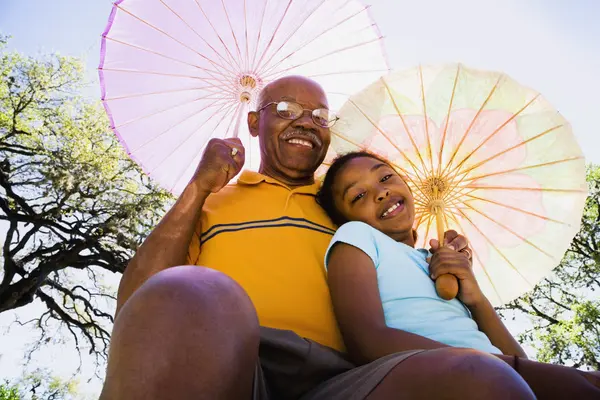 African American grandfather and granddaughter with parasols
