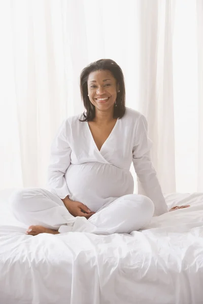 Pregnant African woman sitting on the bed
