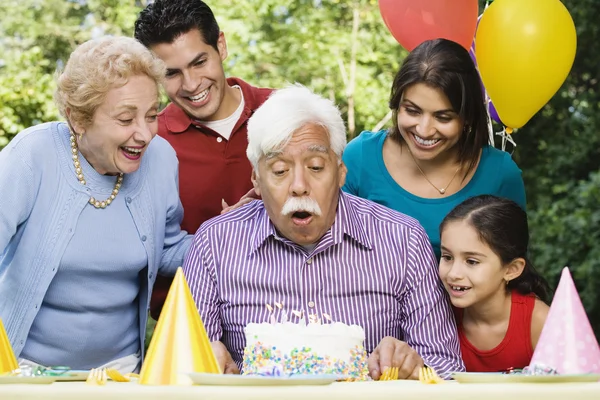 Senior Hispanic man blowing out birthday candles with family in park