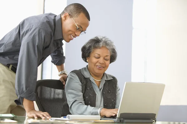 Man leaning over desk of mature woman with computer