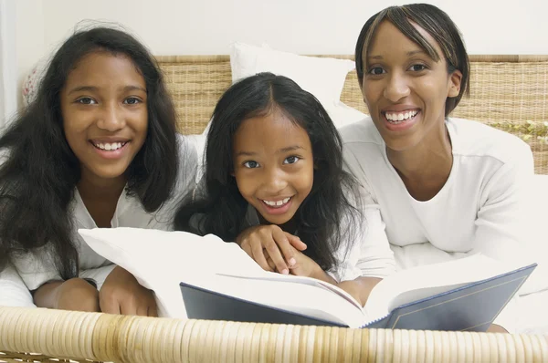 African American mother and daughters on bed with book