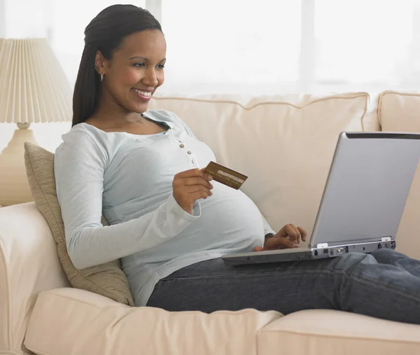 Pregnant African woman shopping online on sofa